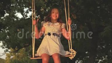 小女孩在阳光下的一棵树下荡秋千，和孩子们玩。 特写镜头。 孩子骑着绳子在秋千上